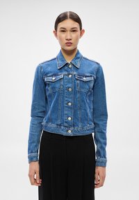 Modrá rifľová bunda s dlhými rukávmi, zapínaním na gombíky vpredu, dvoma náprsníkovými vreckami a skráteným lemom; obsahuje detailné prešívanie a strieborné kovanie.