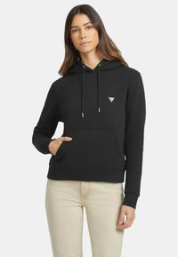 Sudadera negra hecha de material suave, con un bolsillo delantero, cordones ajustables y un pequeño logo triangular en el pecho.