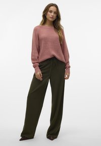 Un pantalon vert olive ample associé à un pull en tricot rose doux et texturé avec un col large et des manches à revers.