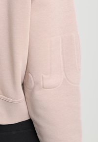 Sweatshirt rose clair présentant une texture côtelée, une coupe décontractée et un logo discret en relief sur la manche. Confectionné en coton doux.