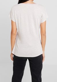 Blusa gris claro de manga corta con un corte relajado, textura suave, escote redondo y aberturas laterales, combinada con pantalones negros.