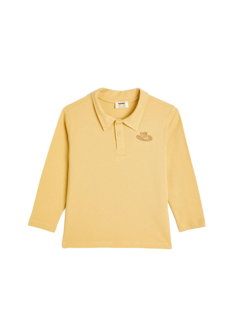Keltainen pitkähihaisen polo-paita, joka on valmistettu pehmeästä puuvillasta ja jossa on kaulus. Paidassa on brodeerattu kuvio vasemmassa rintataskussa.