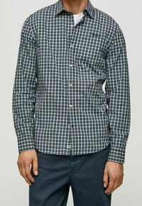 Camicia a maniche lunghe con bottoni in fantasia a quadri verde e bianco, in tessuto di cotone, con colletto classico e bottoni in contrasto.