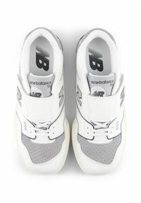 Weißer Sneaker mit grauen Wildleder-Akzenten, perforierter Textur, Gummisohle und Klettverschluss. Enthält das "New Balance"-Logo und die Modellnummer 550.