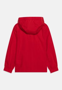 Röd hoodie-jacka med en mjuk textur, elastiska cuffs och huva med dragsko. Slät tyg utan synliga knäppningar eller mönster.