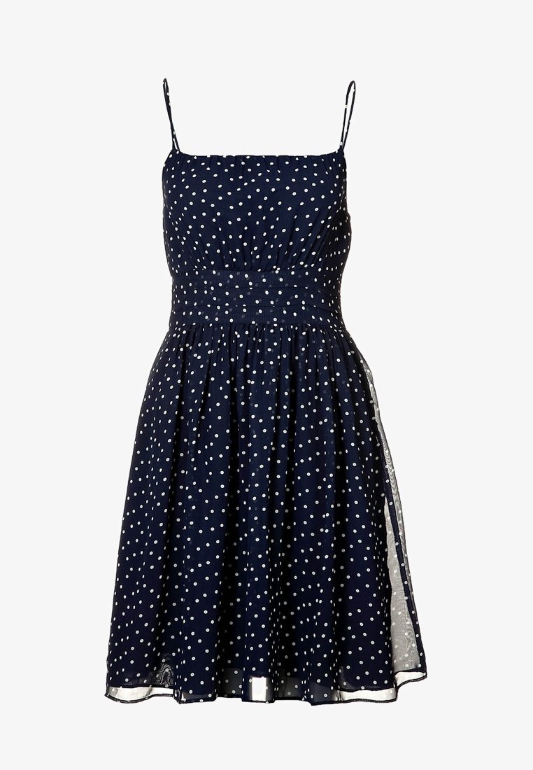 Robe sans manches bleu marine à pois blancs, taille cintrée, bretelles fines et jupe évasée longueur genou.