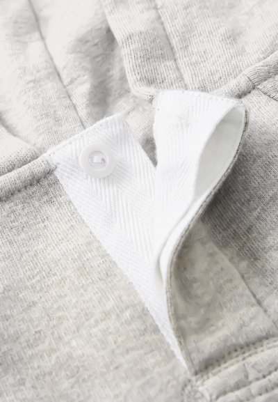 Lähikuva valkoisesta napista, joka on kiinnitetty pintakuviolliseen vaaleanharmaaseen kangasseen, näyttää yksityiskohtaisesti ompeleet ja kankaan kudoksen.