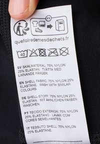 Etichetta di cura su un articolo in tessuto nero; include istruzioni per la cura e dettagli sui materiali: 75% nylon, 25% elastan; testo multilingue.