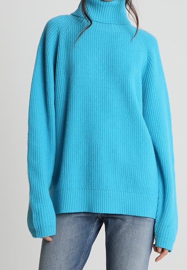 Pull col roulé turquoise avec texture côtelée, coupe décontractée et manches longues, associé à un jean bleu.