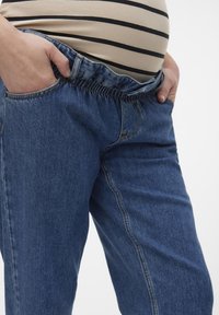 Blå denimgraviditetsjeans med elastisk midja, framfickor och en avslappnad passform. Tyget har en slät, något texturerad yta.