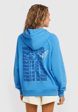 Blauwe kaptrui van zacht materiaal met een decoratieve afbeelding op de achterkant, bestaande uit tekst en golfpatronen in donkerder blauw.