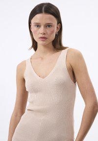 Top in maglia color beige con scollatura a V, dotato di una vestibilità aderente e di un motivo testurizzato verticale. Tessuto liscio con leggero elastico.