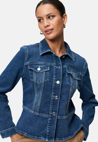 Donkerblauwe denimjas met een knoopsluiting aan de voorkant, twee borstzakken en een gestructureerde pasvorm met lange mouwen en een licht uitlopende zoom.