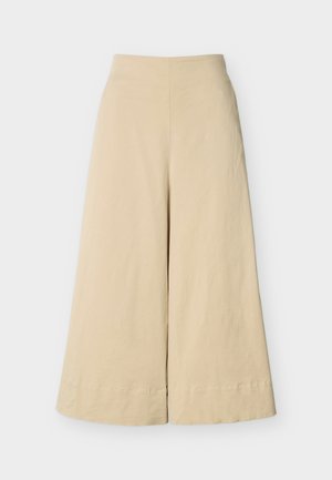 Παντελόνι μπεζ, ψηλόμεσο με φαρδιά μπατζάκια, με λεία υφή και ραμμένες ραφές, απεικονίζεται σε απλό φωτεινό φόντο.