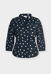 Blouse bleu marine à pois blancs, manches trois-quarts, col et devant croisé.