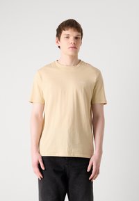 Beige bomulds t-shirt med rund hals og korte ærmer. Har lille "HUGO" logo på venstre bryst. Glat, let tekstur.