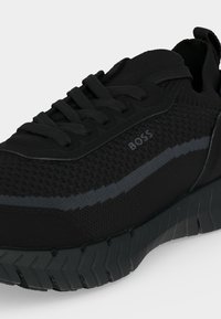 Μαύρο υφασμάτινο sneaker με σχέδιο κορδονιών, παχιά αυλακωτή σόλα και λογότυπο "BOSS" στη πλευρά σε λεπτομέρεια σκουρόχρωμης γκρι ρίγας.