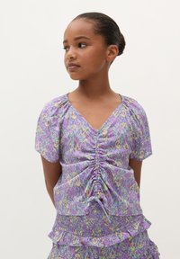 Lila gemusterte Bluse mit kurzen Puffärmeln, V-Ausschnitt, Raffung in der Mitte und gerafftem, rüschendem Saum.