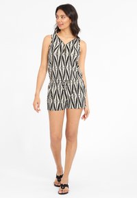 Romper à motifs noir et blanc avec un design sans manches, un col en V, une taille élastique et des shorts. Porté avec des sandales plates noires.