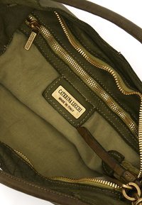 Vista interna di una borsa verde oliva con cerniere in tono oro, fodera in tessuto e un'etichetta che recita "CATERINA LUCCHI MADE IN ITALY."