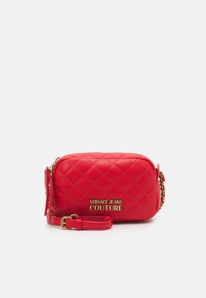 Mała czerwona pikowana torba na ramię z złotym logo „Versace Jeans Couture” i detalem pasek z łańcuszkiem na białym tle.