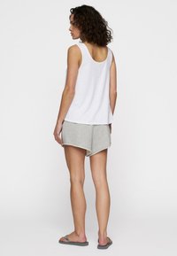 Top blanco sin mangas con escote redondeado, combinado con pantalones cortos grises con dobladillo curvo y un ajuste casual. Tejido texturizado, diseño relajado.