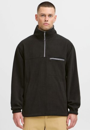 Black fleece pullover with a high collar, half-zip front, and chest pocket. Features cuffed sleeves and a soft, textured surface.