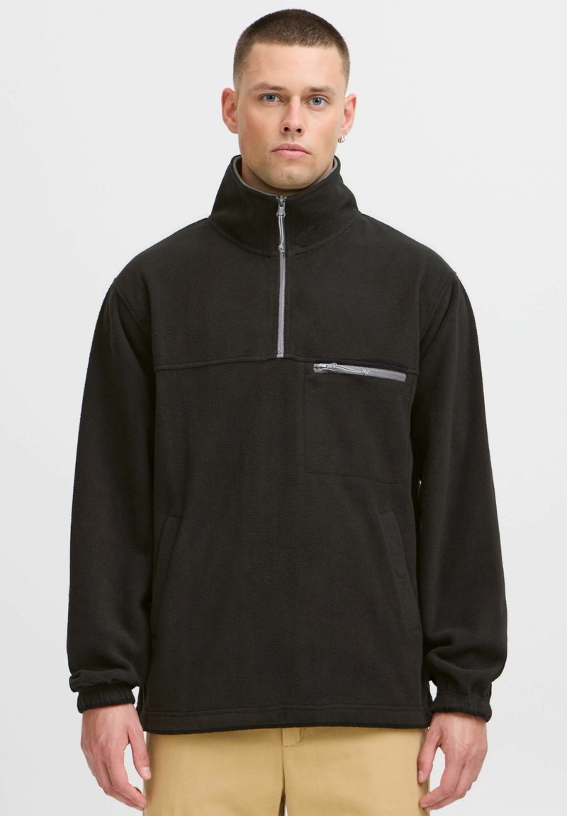 Black fleece pullover with a high collar, half-zip front, and chest pocket. Features cuffed sleeves and a soft, textured surface.