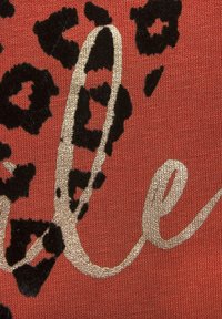 Red fabric with black leopard print and gold foil script detailing. The texture includes plush black accents within the print.