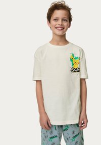 Crèmekleurige t-shirt met een Pikachu-afbeelding en tekst "#0025", gecombineerd met lichtblauwe pyjamabroek die verschillende Pikachu-patronen toont.