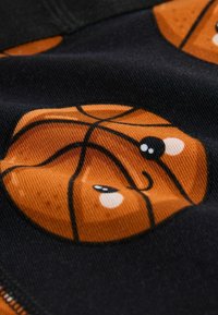 Gros plan sur un tissu avec un graphique de ballon de basket orange présentant un visage mignon avec des yeux et une bouche souriante sur un fond sombre.