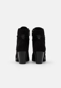 Schwarze Wildleder-Stiefeletten mit hohem Absatz, seitlichem Reißverschluss, dekorativem Schleifendetail und strukturierter Oberfläche.