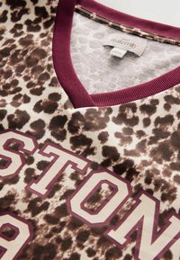 Kortärmad topp med leopardmönster i beige, med en vinröd V-ringning och djärva "BOSTON"-bokstäver i krämvitt och vinrött. Mjuk tygstruktur.