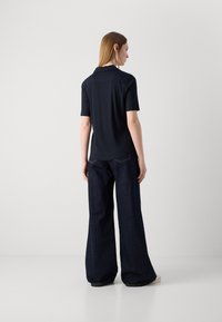 Črna polo majica kratkih rokavov, iz mehkega materiala, s straight hem, v kombinaciji z širokimi temnimi traper hlačami, ki prikazujejo udoben kroj.