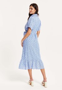 Light blue midi dress with a collar, short puff sleeves, and a ruffled hem. Features floral patterns and a cinched waist with a tie belt.