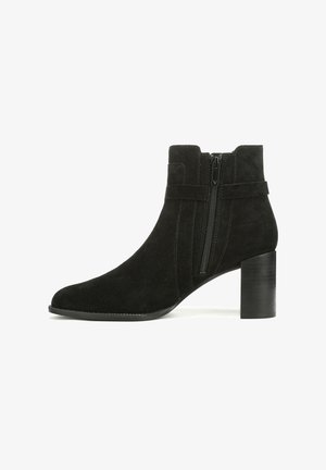 Bottes chelsea en suédine noire avec un nez pointu, une fermeture éclair sur le côté et un talon empilé noir. Présente un design épuré et une surface texturée.
