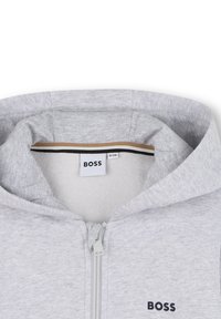 Γκρι φούτερ με κουκούλα και φερμουάρ στο μπροστινό μέρος, με διχτυωτή επένδυση, μαύρες και χρυσές λεπτομέρειες στο εσωτερικό και λογότυπο BOSS στο στήθος.