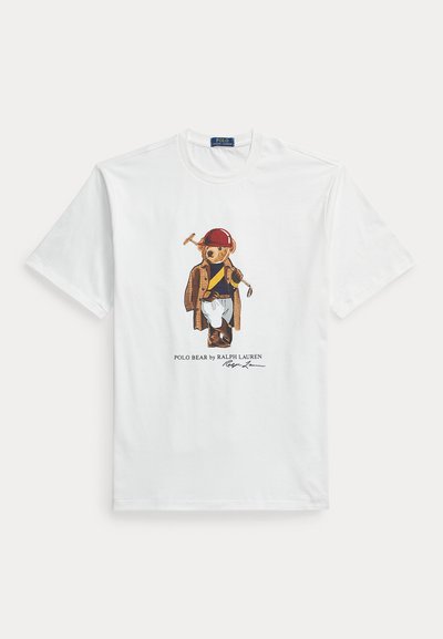 Weißes T-Shirt mit Polo-Bär, der einen roten Polohelm, braune Jacke, blau-gelben Pullover, weiße Hose und braune Stiefel trägt und ein Polo-Schläger hält.