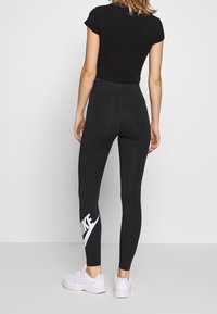Zwarte sportleggings met een hoge taille, voorzien van een opvallend wit Nike-logo op het linkerbeen. Gecombineerd met een aansluitende zwarte crop top en witte sneakers.