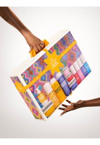 Sett med kroppspleieprodukter i en fargerik mønstret eske med et lyst oransje håndtak, med ulike flaskefasonger og farger.