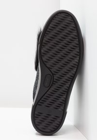 Schwarzer Sneaker mit einem strukturierten Obermaterial aus Stoff und einer gemusterten Gummisohle. Die Sohle hat ein erhabenes, geometrisches Profil für besseren Halt.