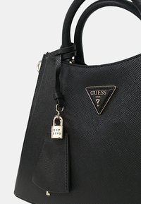 Borsa a tracolla nera in materiale sintetico testurizzato, con logo metallico triangolare e un'etichetta decorativa con la scritta "EST 1981". Presenta manici doppi.