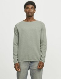 Hellgrüner, strukturierter Strickpullover mit langen Ärmeln und Rundhalsausschnitt, kombiniert mit hellblauen Jeans, auf einem neutralen Hintergrund präsentiert.