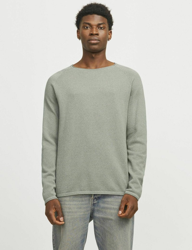 Hellgrüner, strukturierter Strickpullover mit langen Ärmeln und Rundhalsausschnitt, kombiniert mit hellblauen Jeans, auf einem neutralen Hintergrund präsentiert.