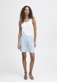 Ljust blå blommiga shorts i mjukt tyg med elastisk midja, som kombineras med en vit ärmlös topp. Klackar fulländar looken.