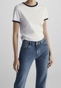 T-shirt bianco in cotone con colletto e polsini a coste blu navy, abbinato a jeans blu in denim a vita alta con tasche anteriori e cerniera.
