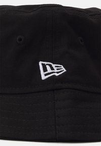 Gorra de cubo negra hecha de tejido texturizado, con un logo bordado blanco en el lado, y con costuras visibles alrededor del ala.