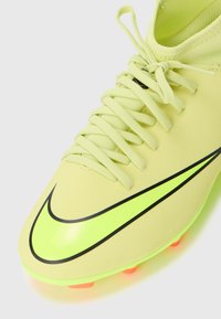 Bota de fútbol Nike en amarillo claro con el logo de swoosh negro, parte superior texturizada, cordones planos y tacos naranjas brillantes en la suela.