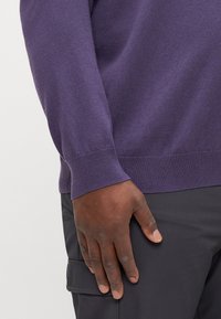 Purple sweater with a crew neck, ribbed cuffs, and hem, worn with black cargo pants; fabric has a soft, smooth texture.