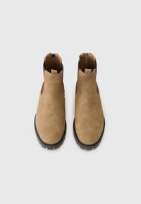 Barna velúr bokapapucs sima felülettel, fekete gumi talppal és oldalsó cipzárakkal. Rugalmas panelekkel ellátva a könnyű felvétel érdekében.